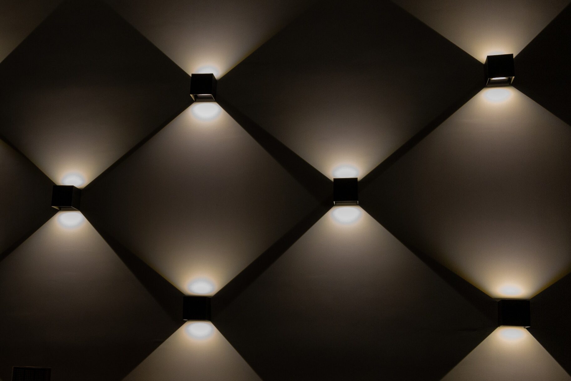 Muro oscuro con retícula geométrica de apliques que proyectan una luz cálida y contenida, símbolo de discreción.